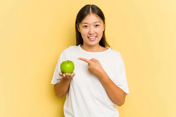 Young Asian Woman Eating Apple Isolated Yellow Background Smiling Pointing — Stock Photo, Image