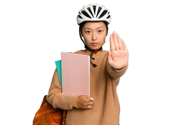 年轻的亚洲学生妇女戴着自行车头盔 与绿色的背景隔离 双手伸出 展示停车标志 阻止了你 — 图库照片