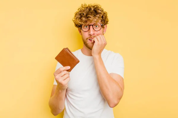 Giovane Uomo Caucasico Possesso Portafoglio Isolato Sfondo Giallo Mordere Unghie — Foto Stock