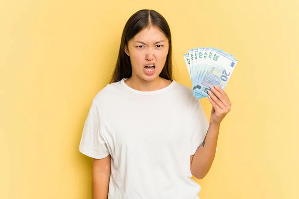 若いアジアの女性は 黄色の背景に孤立した紙幣を持っている非常に怒って積極的に叫んで — ストック写真