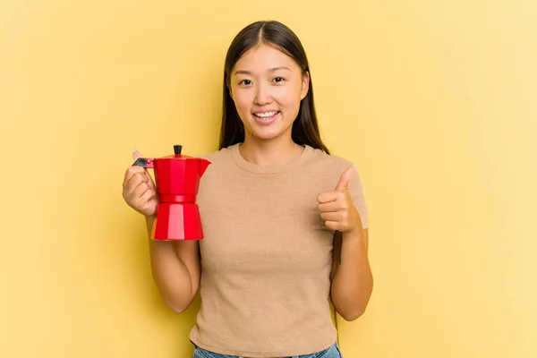 若いですアジアの女性を保持コーヒーメーカー隔離上の黄色の背景笑顔と上げ親指アップ — ストック写真