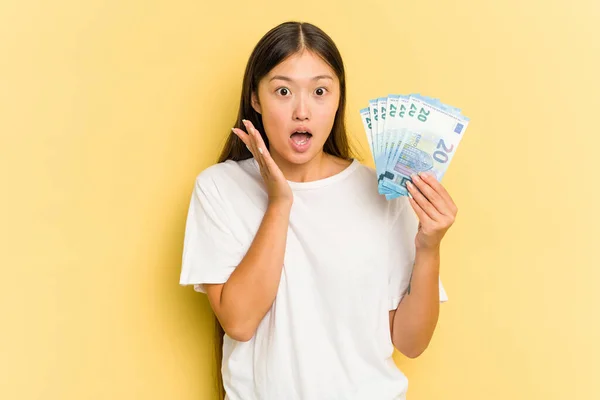 Young Asian Woman Holding Banknotes Isolated Yellow Background Surprised Shocked — Stock Photo, Image