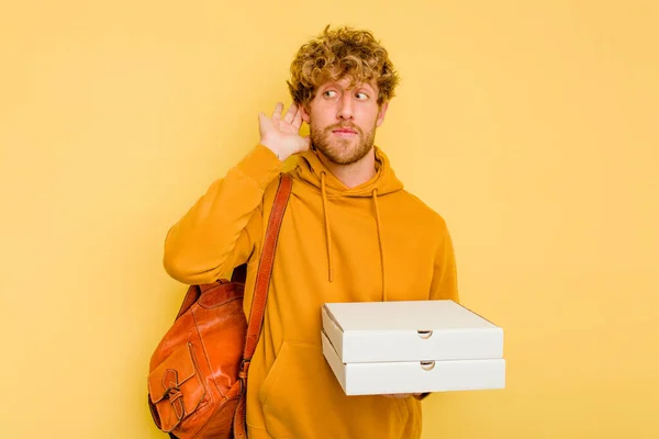 Młody Student Człowiek Trzymając Pizze Izolowane Żółtym Tle Próbuje Słuchać — Zdjęcie stockowe