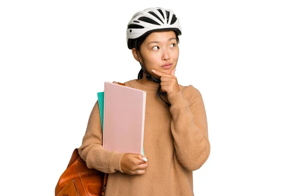 年轻的亚洲学生女子戴着自行车头盔 背景为绿色 侧面看去 脸上带着怀疑和怀疑的表情 — 图库照片
