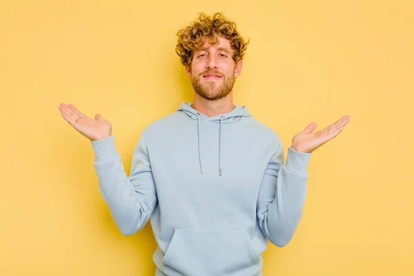 Young Caucasian Man Isolated Yellow Background Makes Scale Arms Feels — Stock Photo, Image