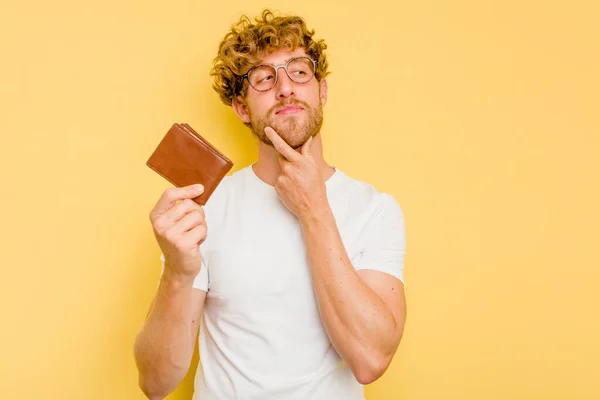 Young Caucasian Man Holding Wallet Isolated Yellow Background Looking Sideways — Stock Photo, Image