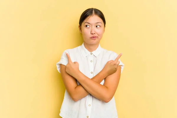 Młoda Azjatka Odizolowana Żółtym Tle Wskazuje Bokiem Próbuje Wybrać Jedną — Zdjęcie stockowe