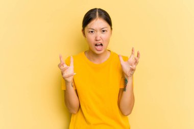 Sarı arka planda izole edilmiş genç Asyalı kadın öfkeyle bağırıyor..
