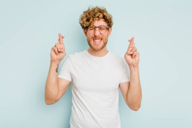 Kafkasyalı genç adam mavi arka planda izole edilmiş şans dilemek için şans diliyor.