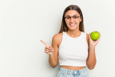 Beyaz arka planda izole edilmiş bir elma tutan genç Hintli kadın gülümsüyor ve boş alanda bir şey gösteriyor..