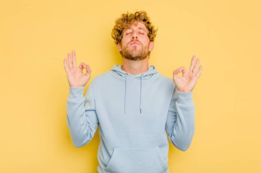 Sarı arka planda izole edilmiş genç beyaz adam sıkı çalışma gününden sonra rahatlıyor. Yoga yapıyor..