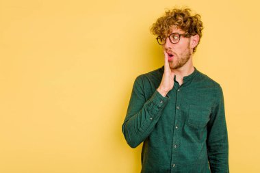 Sarı arka planda izole edilmiş genç beyaz bir adam gizli bir sıcak fren haberi veriyor ve yana bakıyor.