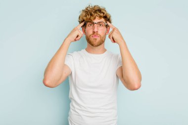 Kafkasyalı genç adam mavi arka planda izole edilmiş bir göreve odaklanmış, parmaklarını işaret ediyor..