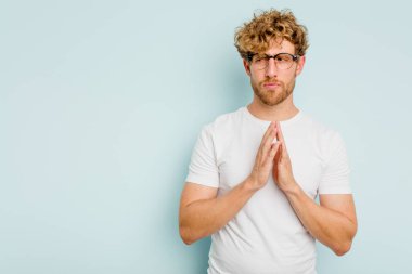 Kafkasyalı genç bir adam mavi arka planda izole edildi. Aklında bir plan kuruyor, bir fikir kuruyor..