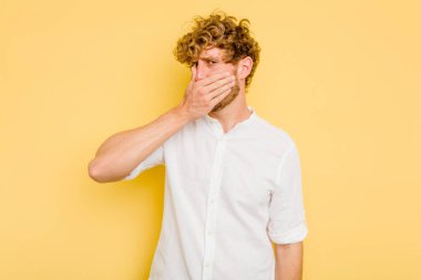 Sarı arka planda izole edilmiş genç beyaz adam elleri endişeli bir şekilde ağzı örtüyor..