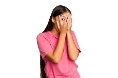 Yeşil krom arka planda izole edilmiş genç Asyalı kadın parmaklarının arasından korkmuş ve gergin bir şekilde göz kırpıyor..