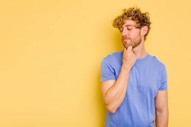 Sarı arka planda izole edilmiş genç beyaz adam şüpheli ve şüpheci bir ifadeyle yana bakıyor..