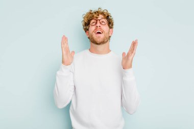 Mavi arka planda izole olmuş genç beyaz adam yüksek sesle gülüyor ve elini göğsüne koyuyor..