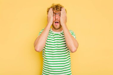 Sarı arka planda izole edilmiş genç beyaz adam yüzünün yarısını palmiye ile örterek eğleniyor..