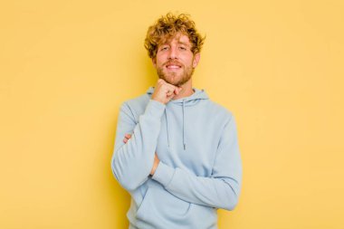 Sarı arka planda izole edilmiş genç, mutlu ve kendinden emin gülümseyen, elleriyle çenesine dokunan beyaz bir adam..