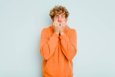 Mavi arka planda izole edilmiş, tırnak yiyen, gergin ve endişeli genç bir beyaz adam..