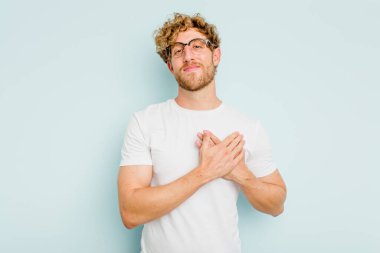 Mavi arka planda izole edilmiş beyaz bir genç, dost bir ifadeye sahip, avuçlarını göğsüne bastırıyor. Aşk konsepti.