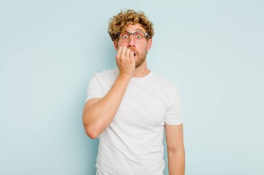 Mavi arka planda izole edilmiş, tırnak yiyen, gergin ve endişeli genç bir beyaz adam..