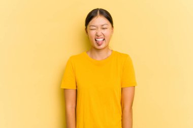 Sarı arka planda izole edilmiş genç Asyalı bir kadın. Komik ve dost canlısı bir dil uzatıyor..