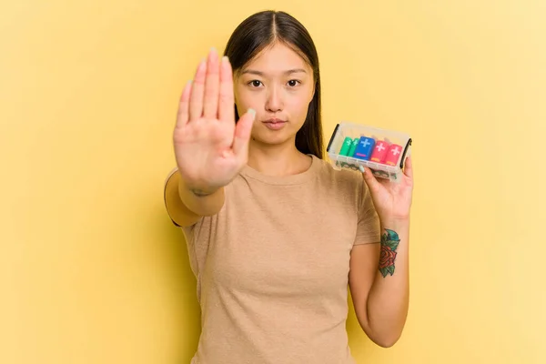 電池を持っている若いアジアの女性は あなたを防ぐために ストップサインを示す延長手で立って黄色の背景に隔離されたリサイクルします — ストック写真