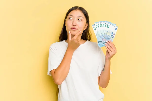 Young Asian Woman Holding Banknotes Isolated Yellow Background Looking Sideways — Stock Photo, Image