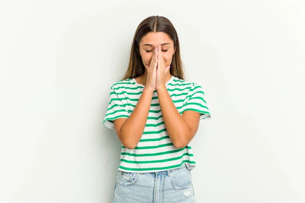 Young Indian woman isolated on white background holding hands in pray near mouth, feels confident.