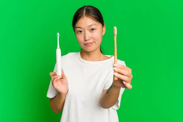 年轻的亚洲女人拿着用绿色底色隔开的电动牙刷 — 图库照片