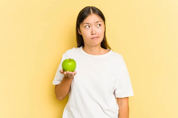 Junge Asiatin Isst Einen Apfel Isoliert Auf Gelbem Hintergrund Verwirrt — Stockfoto