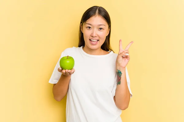배경에 사과를 아시아 소녀는 손가락으로 평화의 상징을 기쁘고 태연하게 보여준다 — 스톡 사진