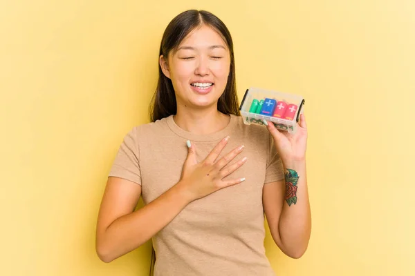 若いアジアの女性は電池を持っているそれらをリサイクルする黄色の背景に隔離された笑い大声で胸に手を保つ — ストック写真