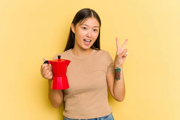 Junge Asiatin Hält Kaffeemaschine Isoliert Auf Gelbem Hintergrund Und Zeigt — Stockfoto