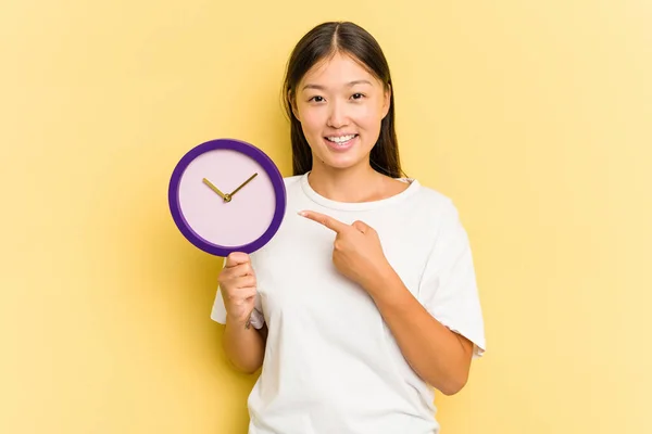 Joven Asiática Sosteniendo Reloj Aislado Sobre Fondo Amarillo Sonriendo Señalando —  Fotos de Stock