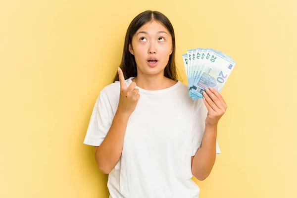 Young Asian Woman Holding Banknotes Isolated Yellow Background Pointing Upside — Stock Photo, Image