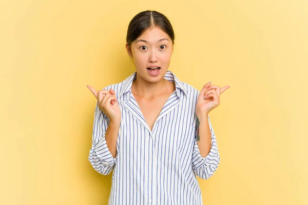 年轻的亚洲女人被黄色背景隔离 指向不同的复制空间 选择其中一个 用手指显示出来 — 图库照片