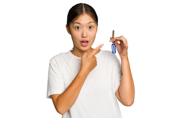 年轻的亚洲女人拿着家里的钥匙 用绿色的色调背景隔开 指向侧面 — 图库照片