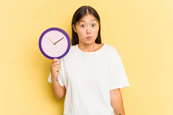 Joven Mujer Asiática Sosteniendo Reloj Aislado Sobre Fondo Amarillo Encoge — Foto de Stock