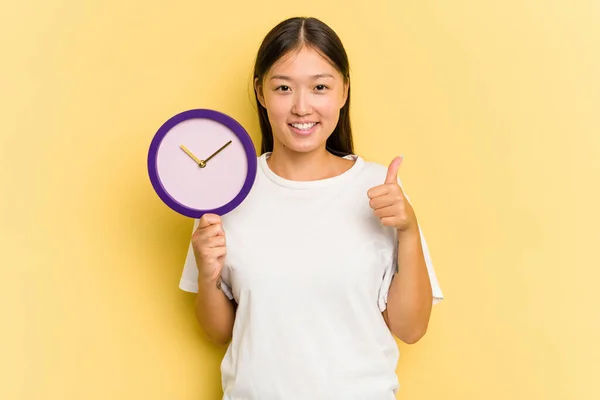 Joven Asiática Sosteniendo Reloj Aislado Sobre Fondo Amarillo Sonriendo Levantando — Foto de Stock