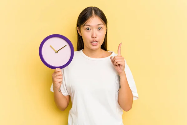 Joven Asiática Sosteniendo Reloj Aislado Sobre Fondo Amarillo Teniendo Alguna —  Fotos de Stock