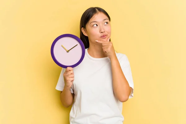 Joven Asiática Sosteniendo Reloj Aislado Sobre Fondo Amarillo Mirando Lado — Foto de Stock