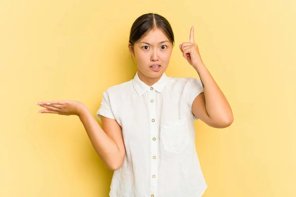 Młoda Azjatka Odizolowana Żółtym Tle Gospodarstwa Pokazując Produkt Rękę — Zdjęcie stockowe