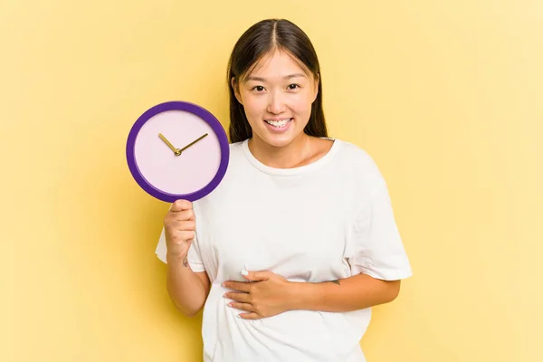 Young Asian Woman Holding Clock Isolated Yellow Background Laughing Having — Stock Photo, Image