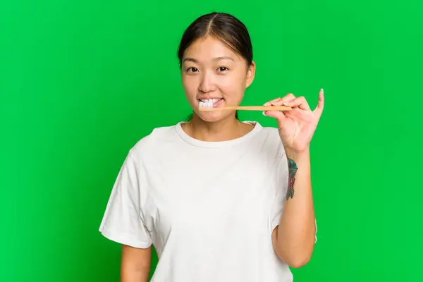 年轻的亚洲女人拿着用绿色底色隔开的电动牙刷 — 图库照片