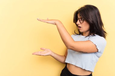 Sarı arka planda izole edilmiş genç Hintli kadın elleri arasında bir kopya alanı tutarken şok ve hayrete düştü..