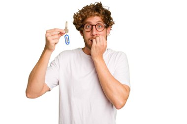 Beyaz arka planda izole edilmiş, tırnak yiyen, gergin ve tedirgin genç beyaz bir adam ev anahtarlarını elinde tutuyor..