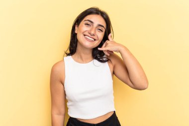 Sarı arka planda izole edilmiş genç Hintli kadın parmakları olan bir cep telefonu hareketi gösteriyor..